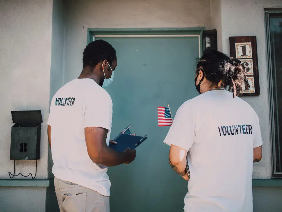 Two masked volunteers in volunteer T-shirts reviewing a clipboard at a front door