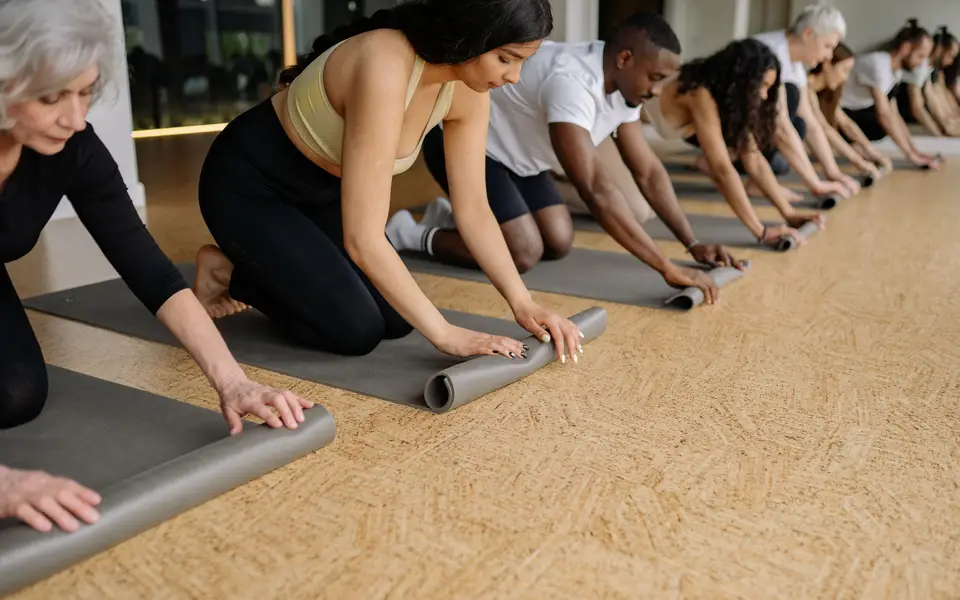 A diverse group of adults rolling yoga mats in a studio before practice, promoting fitness and wellbeing.