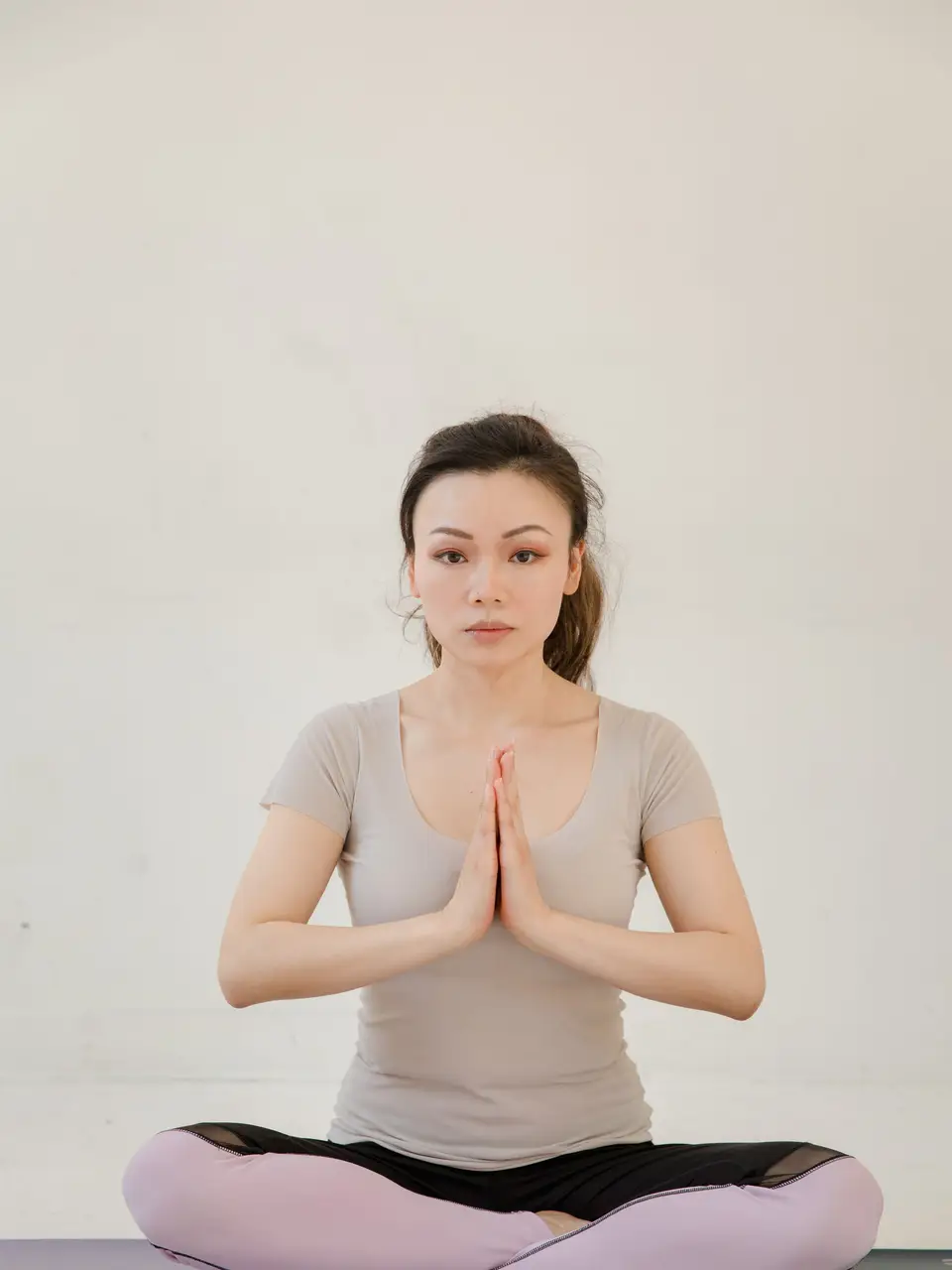 A serene Asian woman practicing yoga indoors, seated in a meditative pose on a mat.