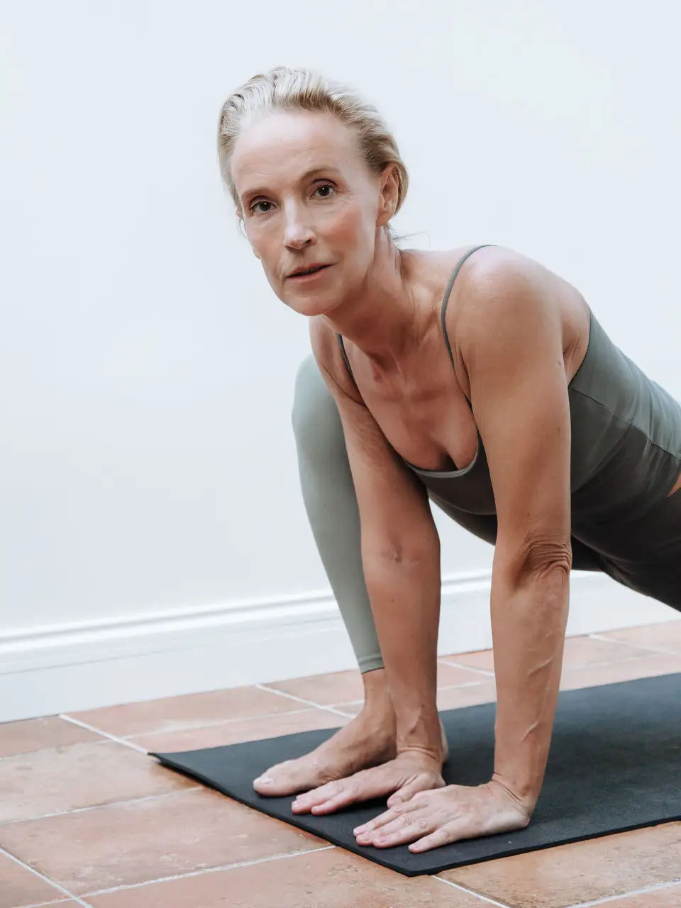 Senior woman in sportswear performing yoga on a mat indoors, demonstrating fitness and health.