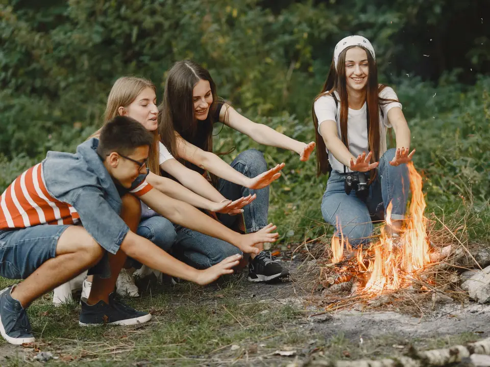 Teens gathered around a campfire under the trees